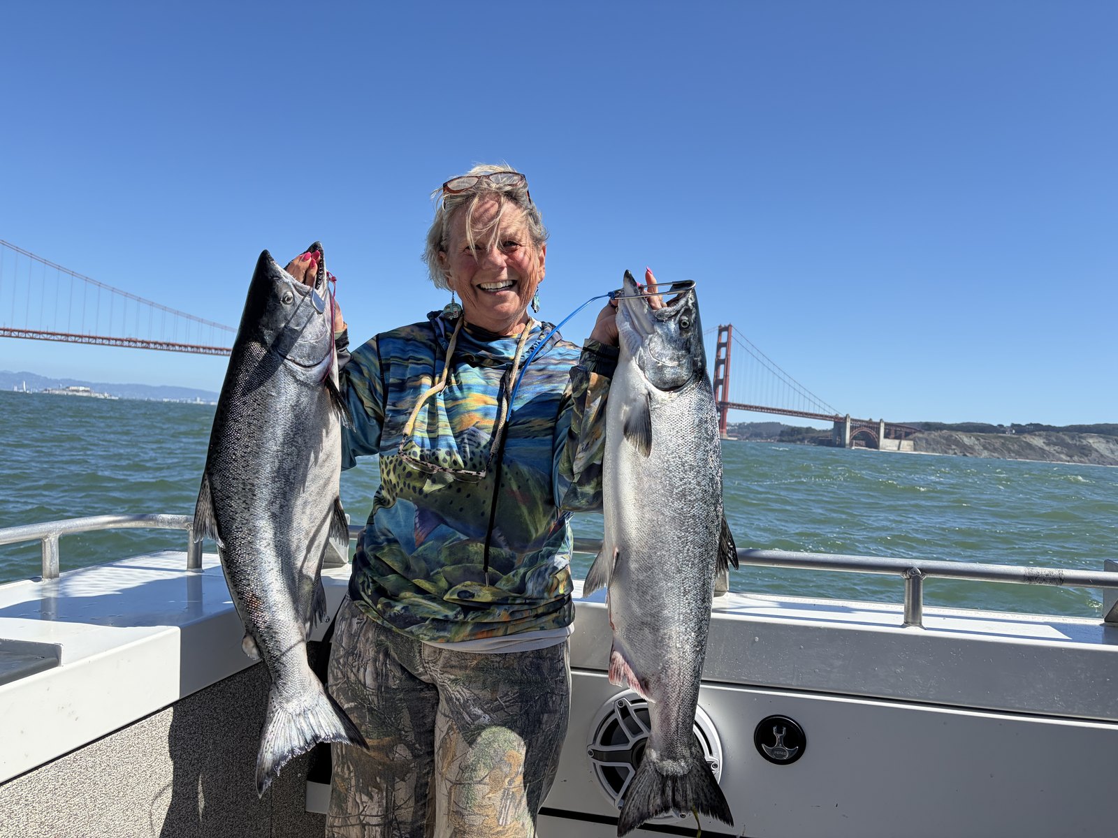 An angler holding two salmon with the Golden Gate Bridge behind