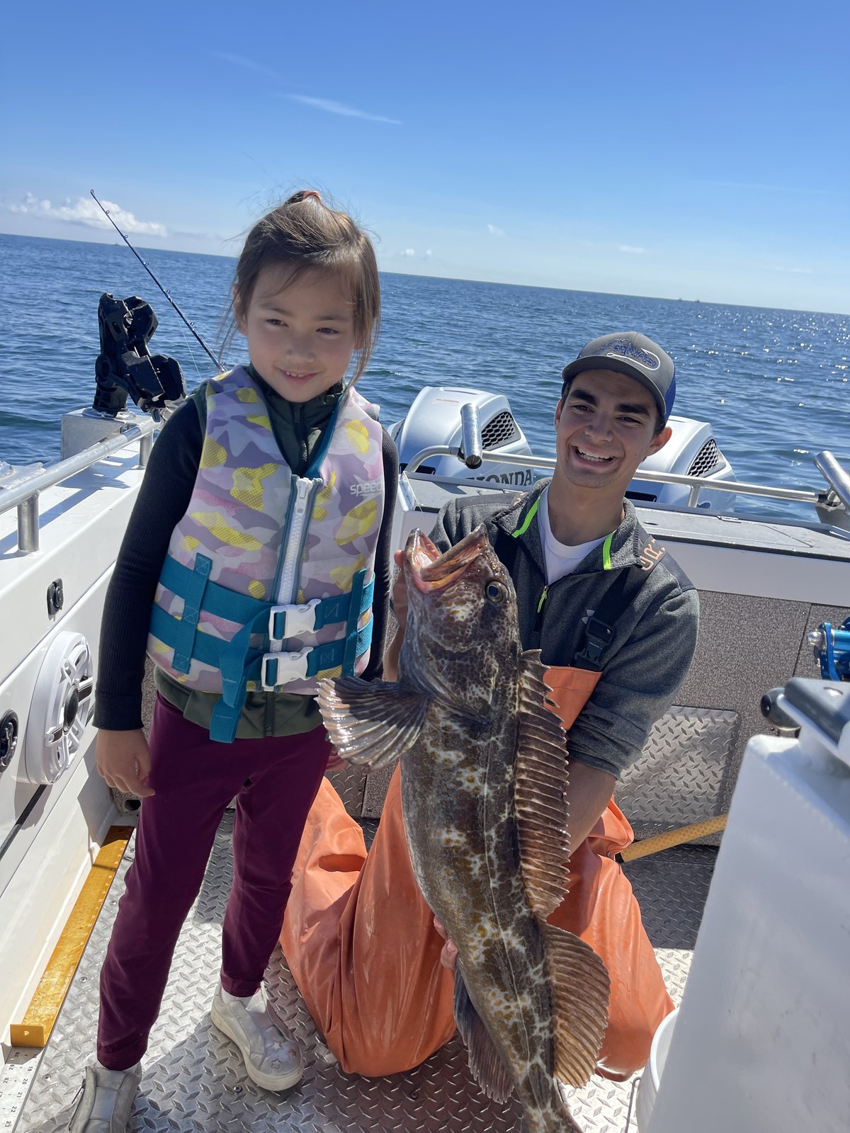 A young angler in a life jacket showing off a lingcod on Fish Invader